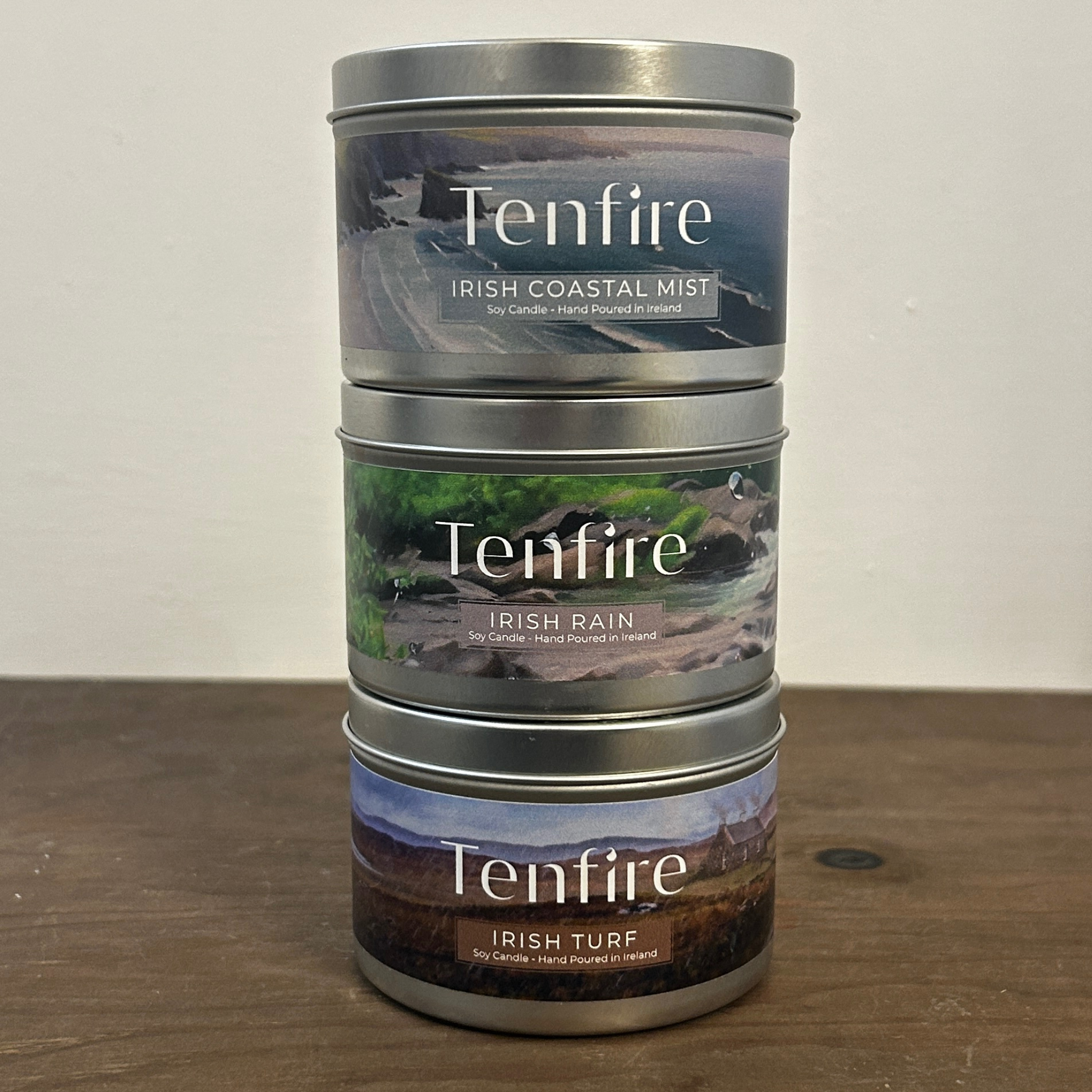 Three silver candle tins stacked called Irish coastal mist, Irish rain and Irish turf all standing on a wooden board