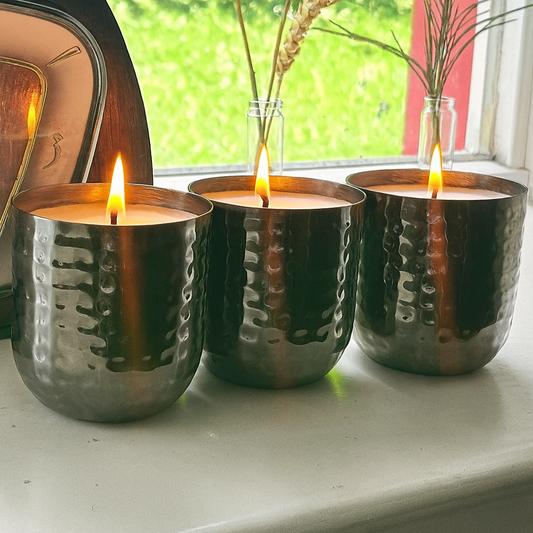 Three lit candles in metallic holders on a windowsill with natural light.