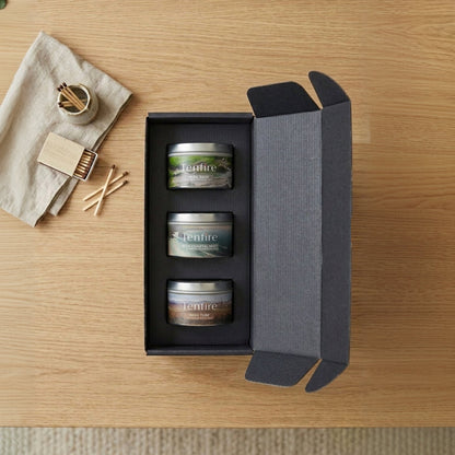 Three small containers in a black gift box on a wooden surface with a towel and matches.