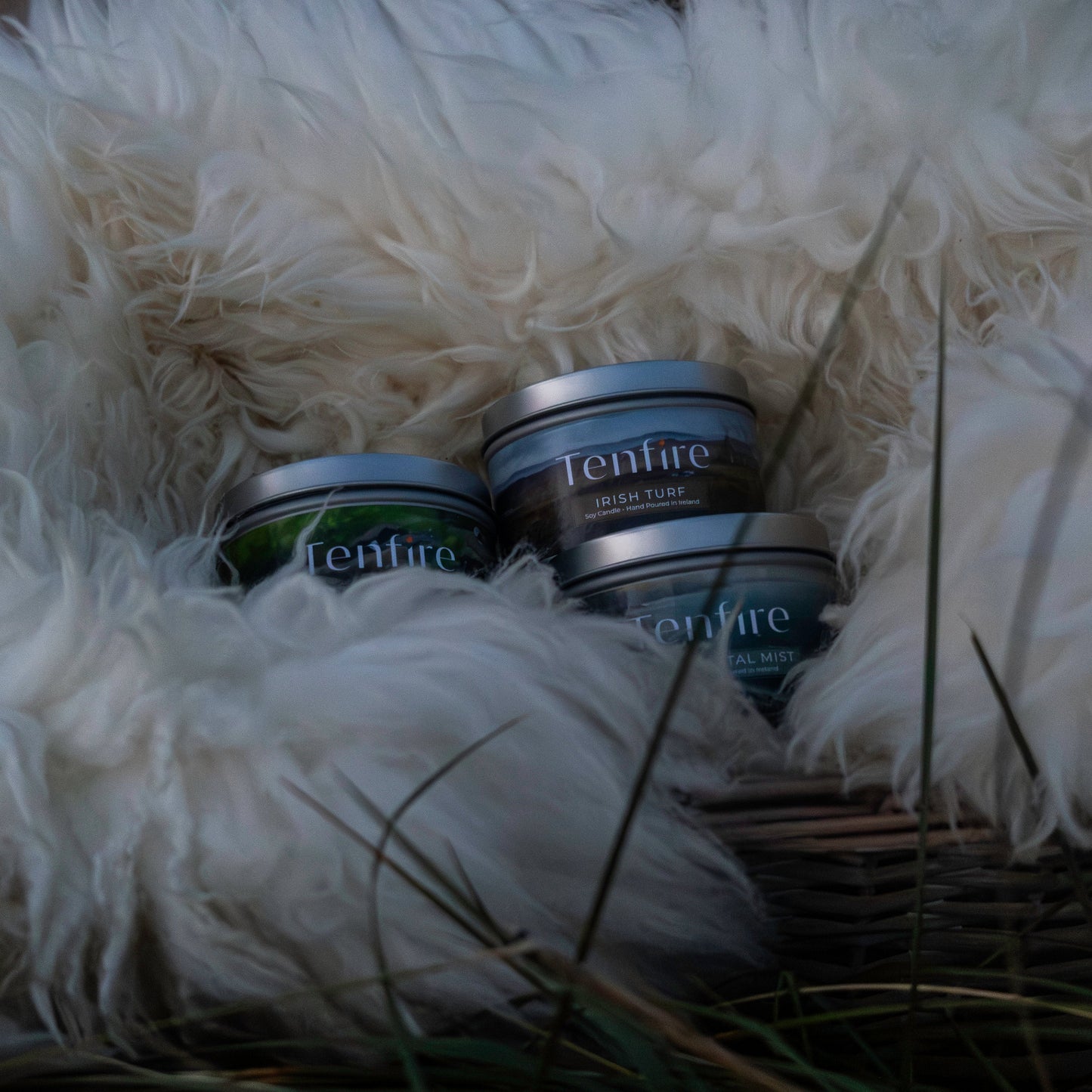 Three tins of Tenfire candles from the Irish Gift Set on a white fluffy surface with grass.