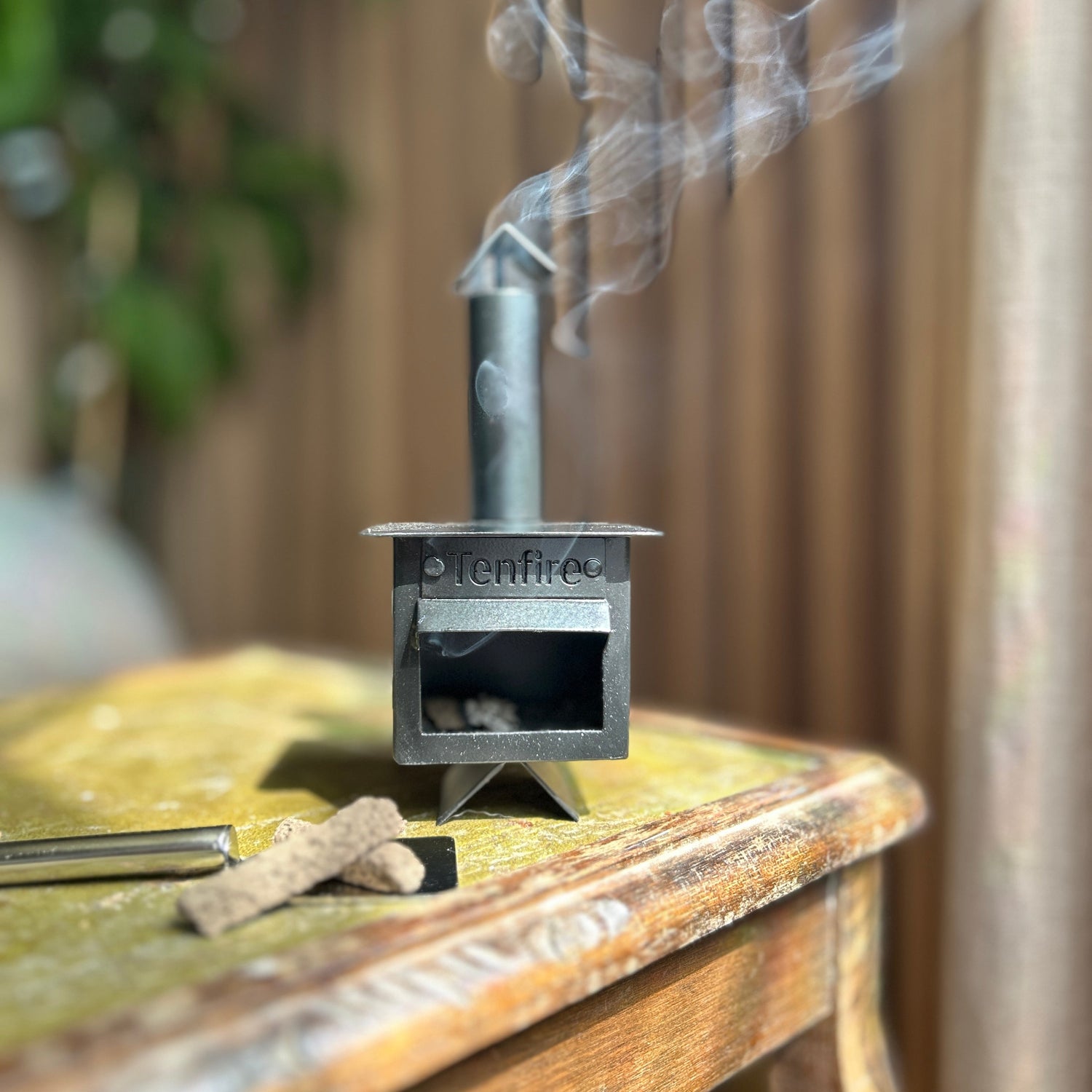 Small metal stove emitting smoke on a wooden surface with a blurred background