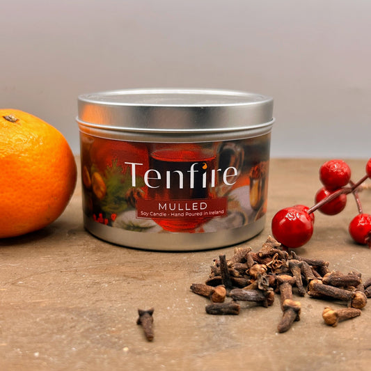 Tenfire mulled candle in a tin with an orange, spices, and berries on a wooden surface.